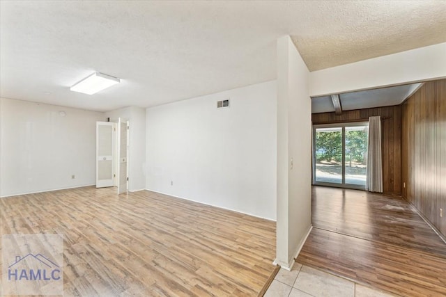 unfurnished room with beamed ceiling, a textured ceiling, light wood-type flooring, and wood walls