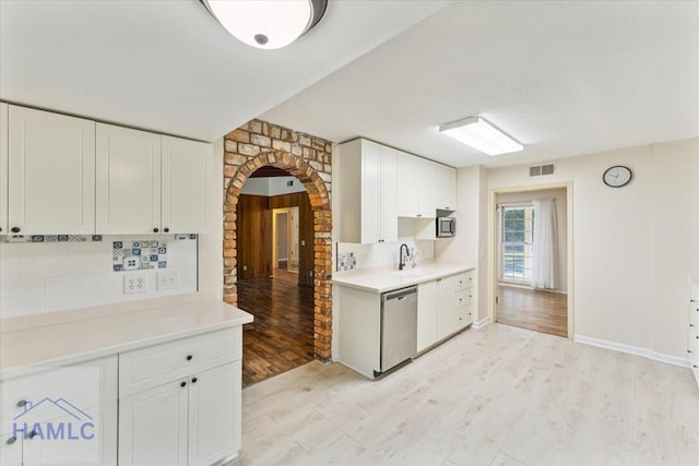 kitchen with stainless steel appliances, tasteful backsplash, light hardwood / wood-style flooring, brick wall, and white cabinets