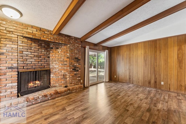 unfurnished living room with beamed ceiling, hardwood / wood-style floors, a textured ceiling, wooden walls, and a fireplace