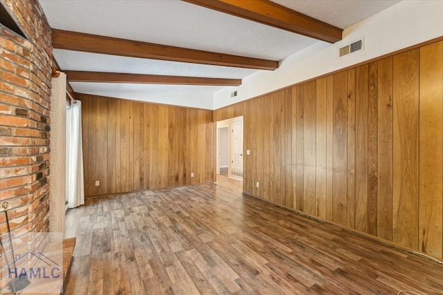 empty room featuring hardwood / wood-style floors, vaulted ceiling with beams, and wooden walls