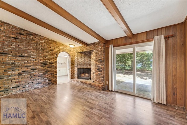 unfurnished living room with lofted ceiling with beams, brick wall, wood walls, a fireplace, and hardwood / wood-style flooring