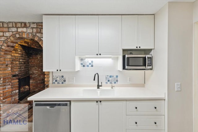 kitchen featuring backsplash, white cabinets, sink, a brick fireplace, and stainless steel appliances