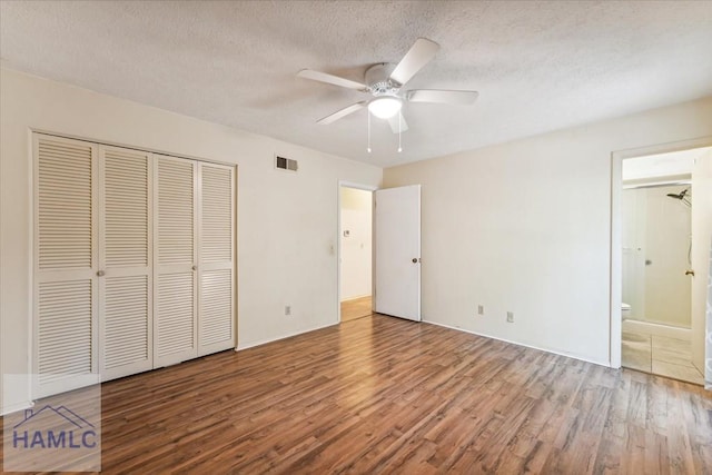 unfurnished bedroom with light wood-type flooring, ensuite bathroom, a textured ceiling, ceiling fan, and a closet