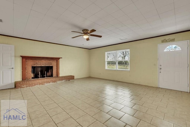 unfurnished living room with ceiling fan, a brick fireplace, brick wall, crown molding, and light tile patterned floors