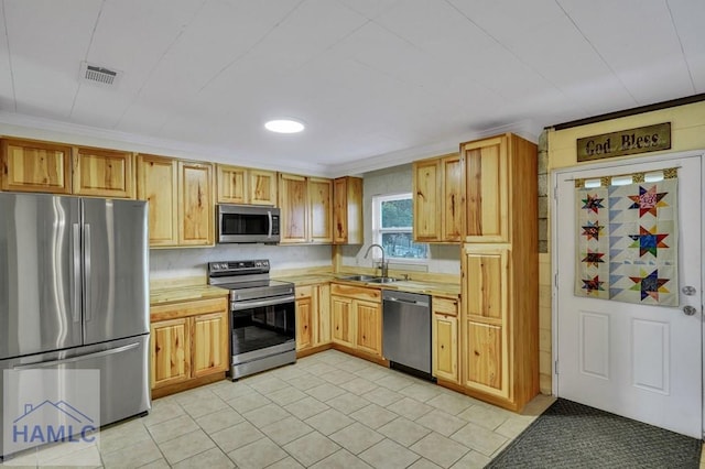 kitchen with light tile patterned floors, stainless steel appliances, crown molding, and sink