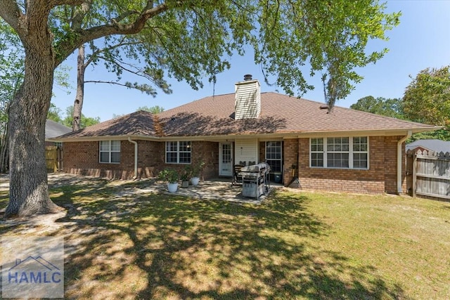 rear view of house with brick siding, fence, a yard, and a chimney