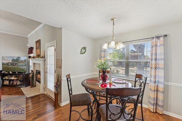 dining space with a textured ceiling, a fireplace, wood finished floors, and a notable chandelier