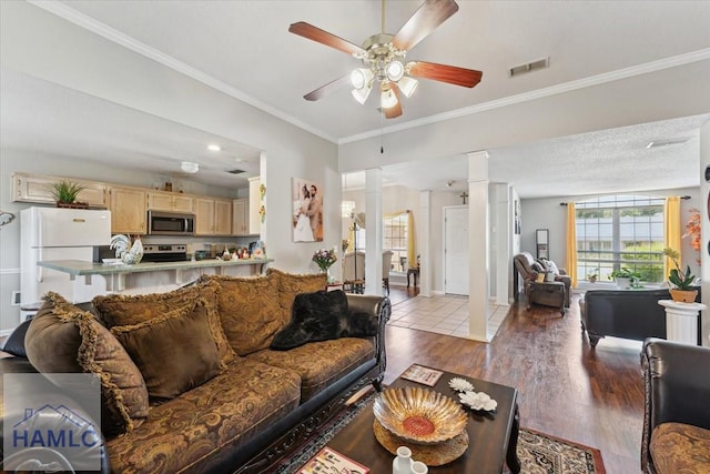 living area with visible vents, crown molding, wood finished floors, ornate columns, and a ceiling fan
