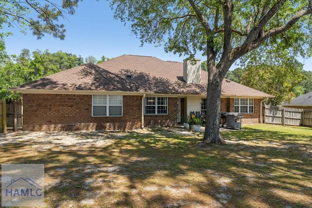 back of property with fence, a chimney, a lawn, and brick siding