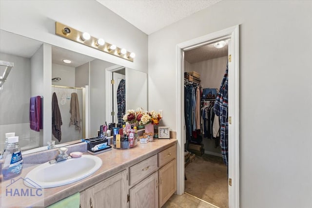 full bathroom with vanity, a shower stall, a textured ceiling, and a spacious closet