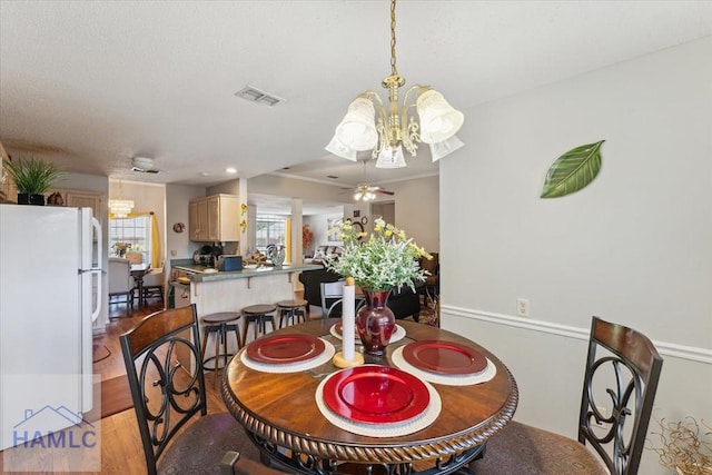 dining space featuring visible vents, light wood-style flooring, and ceiling fan with notable chandelier
