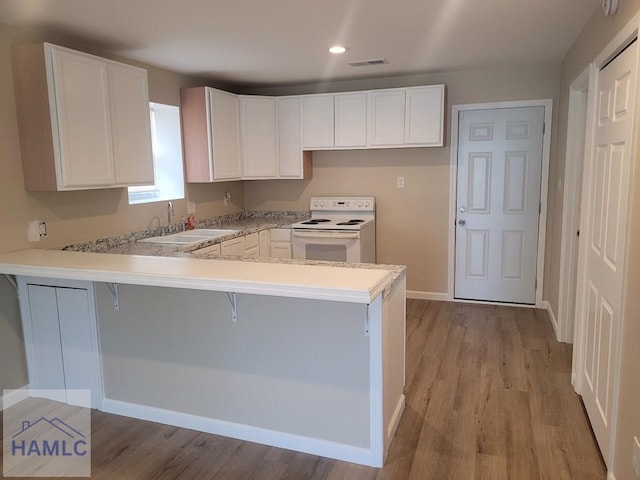 2922 7th St, Columbus, GA 31906 - kitchen featuring white range with electric stovetop, a peninsula, light wood-type flooring, a breakfast bar area, and recessed lighting