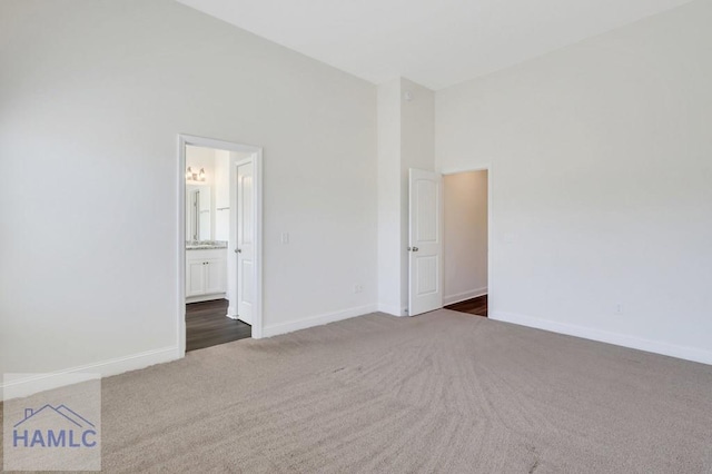 unfurnished bedroom featuring dark colored carpet, a towering ceiling, and ensuite bath