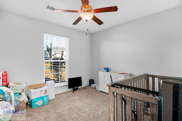 carpeted bedroom with ceiling fan and a crib