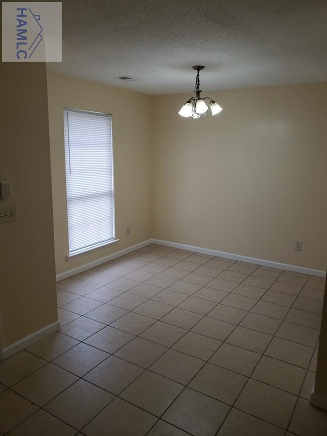 spare room with light tile patterned flooring, a textured ceiling, and a notable chandelier