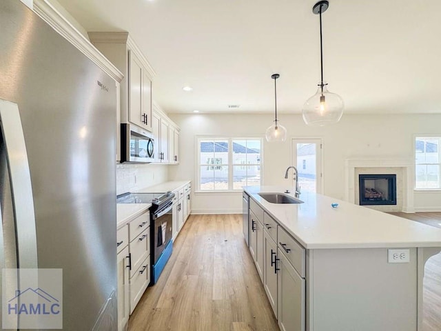 kitchen with stainless steel appliances, sink, decorative light fixtures, white cabinetry, and an island with sink