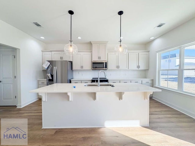 kitchen with white cabinets, a center island with sink, sink, decorative light fixtures, and stainless steel appliances