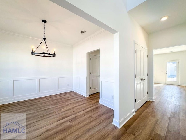 unfurnished dining area featuring hardwood / wood-style floors, an inviting chandelier, and crown molding