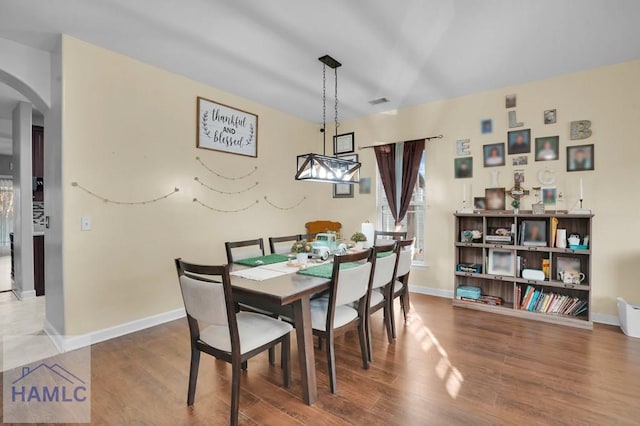 dining room with wood finished floors, arched walkways, and baseboards