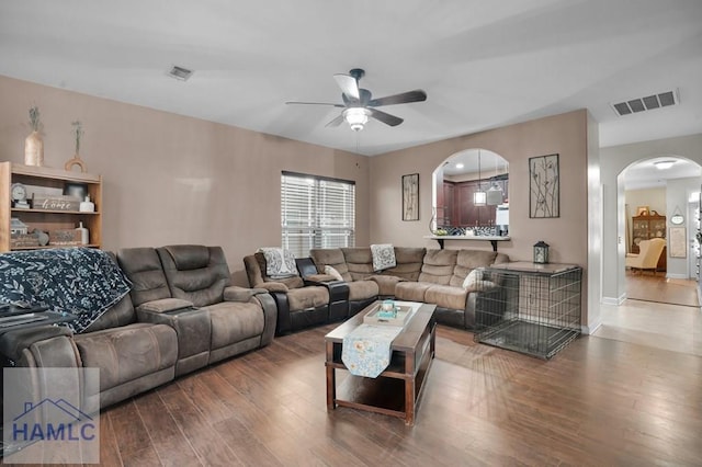 living area featuring arched walkways, visible vents, ceiling fan, and wood finished floors