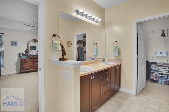 bathroom with tile patterned flooring, a walk in closet, baseboards, double vanity, and a sink