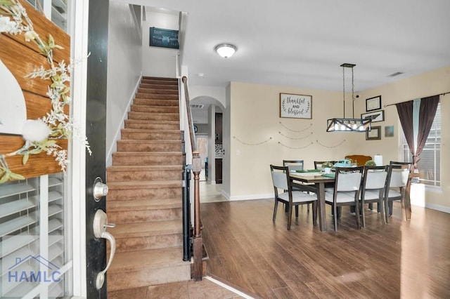 dining area with arched walkways, visible vents, stairs, and wood finished floors