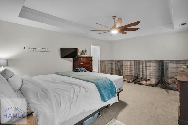 carpeted bedroom with a tray ceiling, visible vents, and ceiling fan