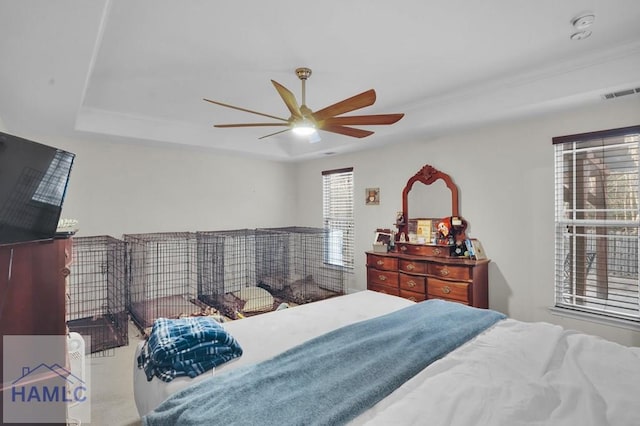 bedroom with a tray ceiling, visible vents, and ceiling fan