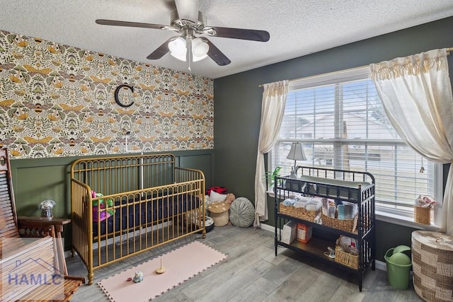 bedroom with a crib, hardwood / wood-style floors, a textured ceiling, and ceiling fan