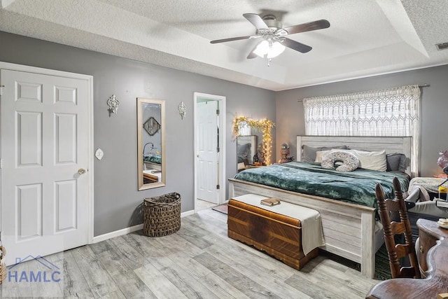 bedroom with a raised ceiling, ceiling fan, a textured ceiling, and light wood-type flooring