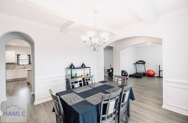 dining space with light wood-type flooring, ornamental molding, sink, beam ceiling, and an inviting chandelier