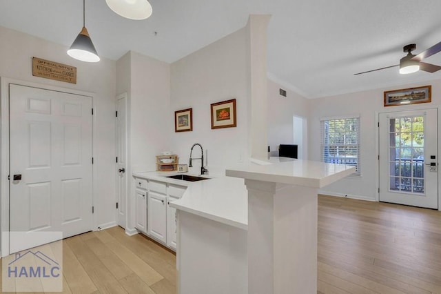 kitchen featuring sink, white cabinetry, light hardwood / wood-style flooring, kitchen peninsula, and pendant lighting