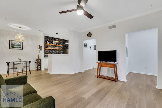 living room with light hardwood / wood-style flooring, ornamental molding, ceiling fan, and indoor bar