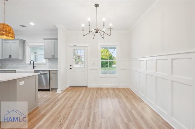 kitchen with stainless steel dishwasher, a notable chandelier, backsplash, decorative light fixtures, and light wood-type flooring