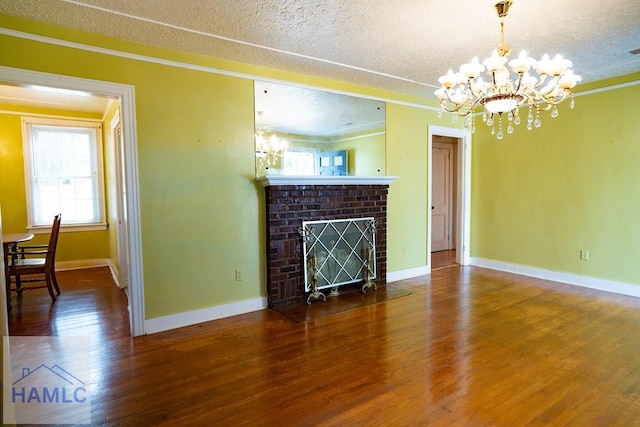 unfurnished living room featuring a textured ceiling, a notable chandelier, wood finished floors, ornamental molding, and a brick fireplace