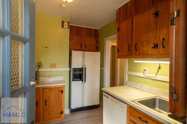 kitchen featuring a textured ceiling, white appliances, light wood-style floors, light countertops, and brown cabinets