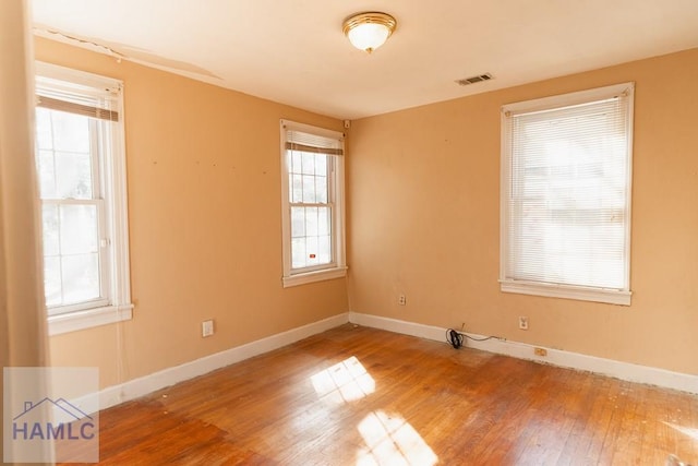 empty room with wood-type flooring, visible vents, and baseboards