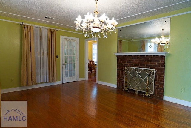 unfurnished living room featuring baseboards, wood finished floors, a textured ceiling, a brick fireplace, and a chandelier