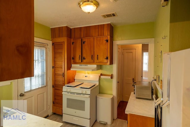 kitchen featuring brown cabinets, light countertops, visible vents, white appliances, and under cabinet range hood