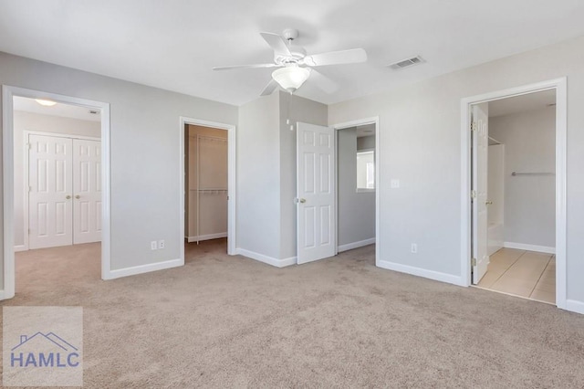 unfurnished bedroom featuring ensuite bath, ceiling fan, light carpet, a walk in closet, and a closet