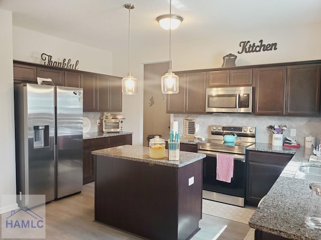 kitchen featuring stainless steel appliances, a kitchen island, pendant lighting, and light stone counters