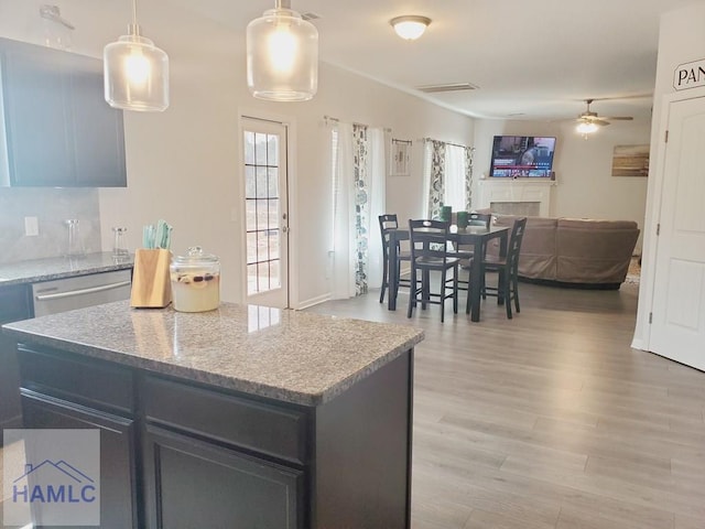 kitchen with a kitchen island, hanging light fixtures, stainless steel dishwasher, light stone counters, and light hardwood / wood-style floors