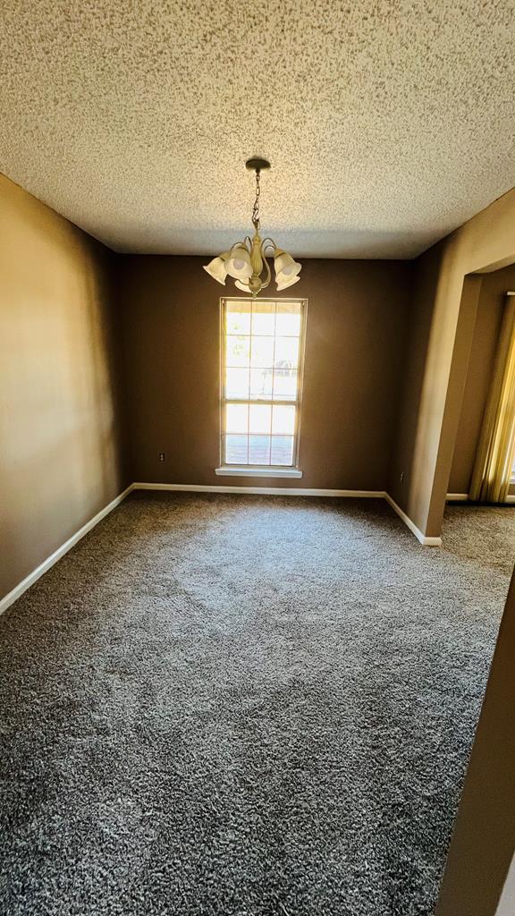 carpeted empty room featuring a chandelier and a textured ceiling