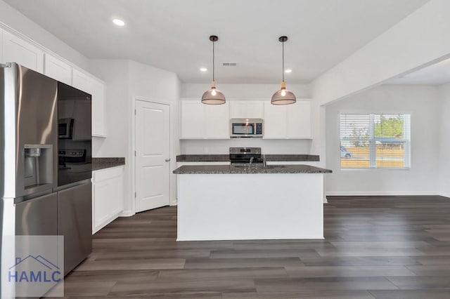 kitchen with decorative light fixtures, a center island with sink, stainless steel appliances, white cabinetry, and dark stone countertops