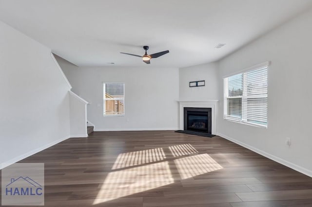 unfurnished living room featuring baseboards, visible vents, dark wood finished floors, a glass covered fireplace, and stairs