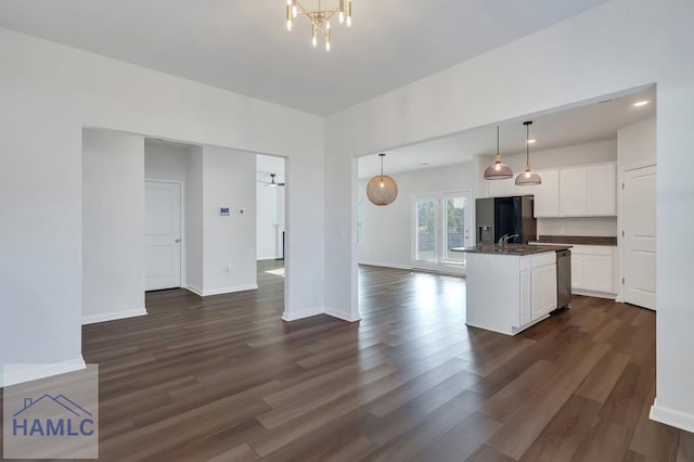 kitchen with pendant lighting, dark countertops, open floor plan, white cabinets, and an island with sink