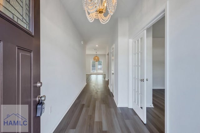 corridor featuring dark wood-type flooring, a chandelier, and baseboards