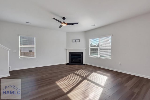 unfurnished living room featuring dark wood-type flooring, a glass covered fireplace, visible vents, and baseboards