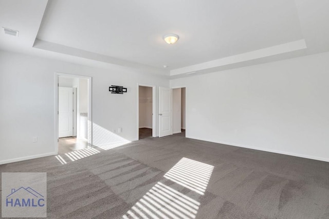 empty room featuring dark carpet, a raised ceiling, visible vents, and baseboards