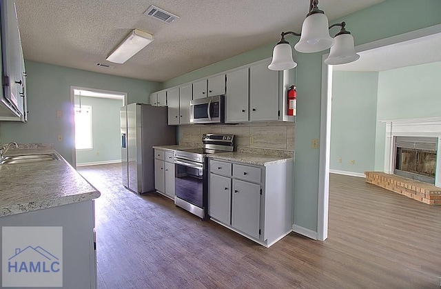 kitchen with appliances with stainless steel finishes, decorative light fixtures, sink, backsplash, and a brick fireplace